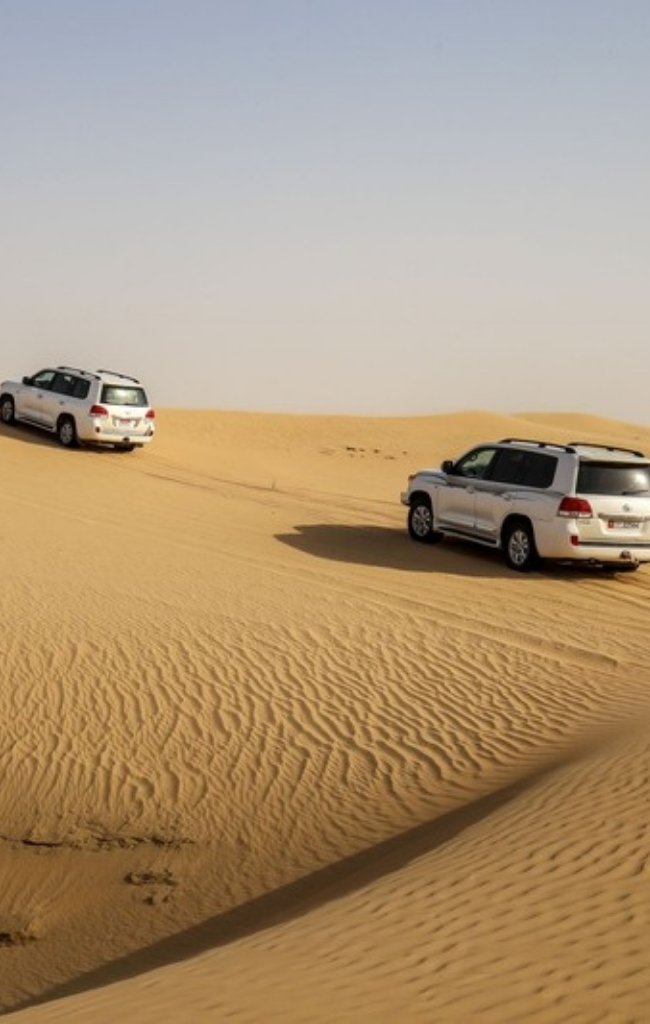 Two 4x4 vehicles driving over golden dunes