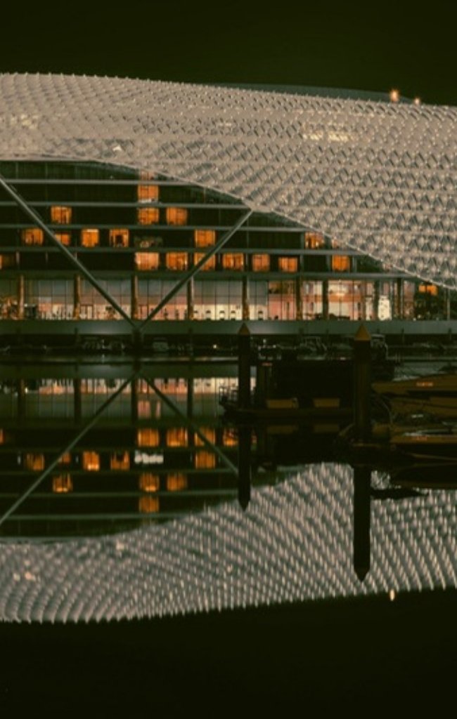 A hotel with a lit lattice canopy reflected in the marina on Yas Island