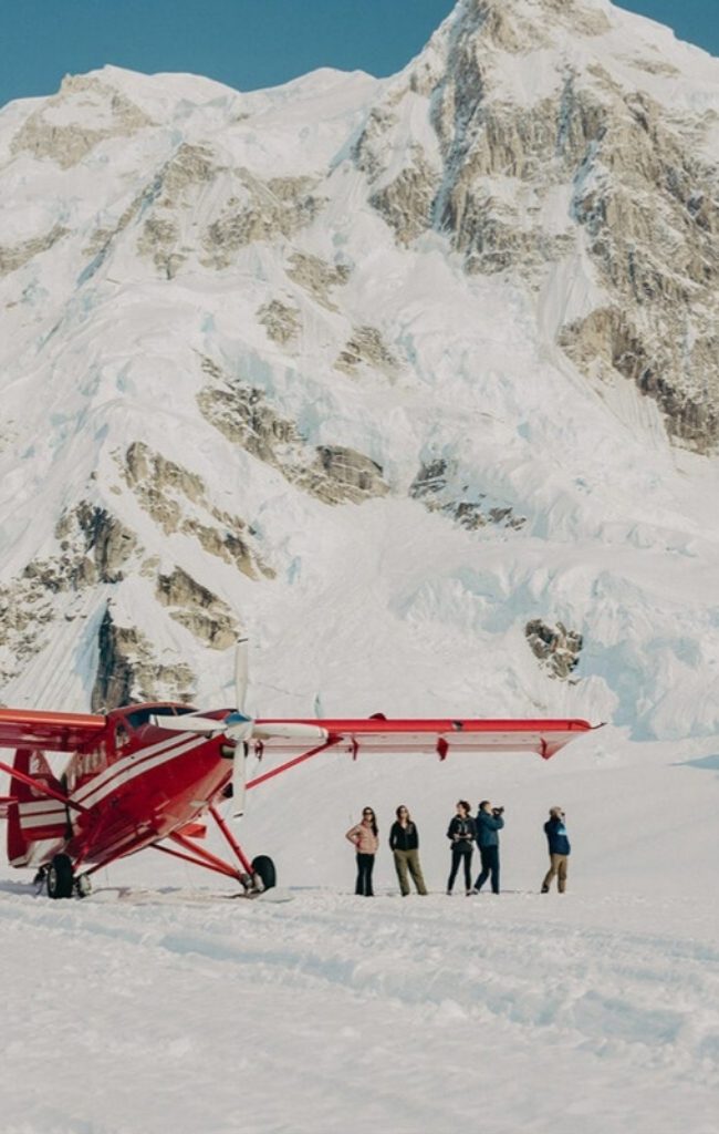 Travelers beside a ski plane after a glacier landing near Denali