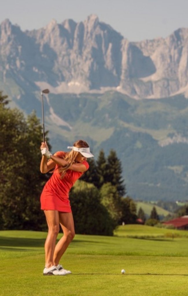A golfer teeing off below the Wilder Kaiser mountains