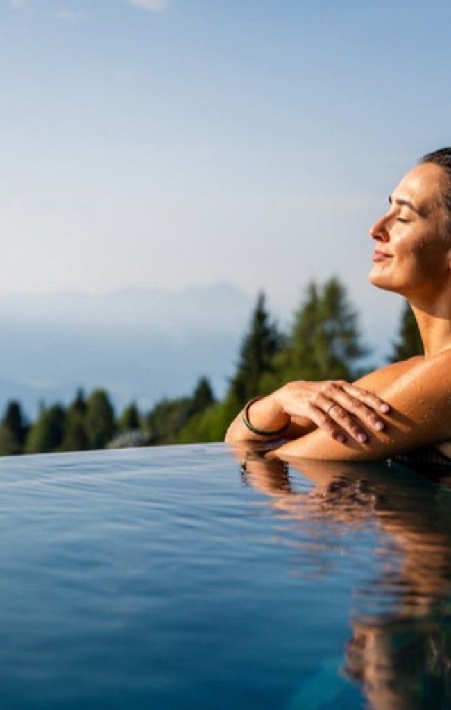 A woman relaxing in an infinity pool above forested mountains