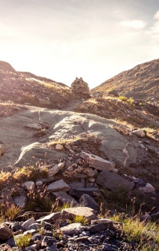 A stone cairn on a sunlit Alpine hiking trail