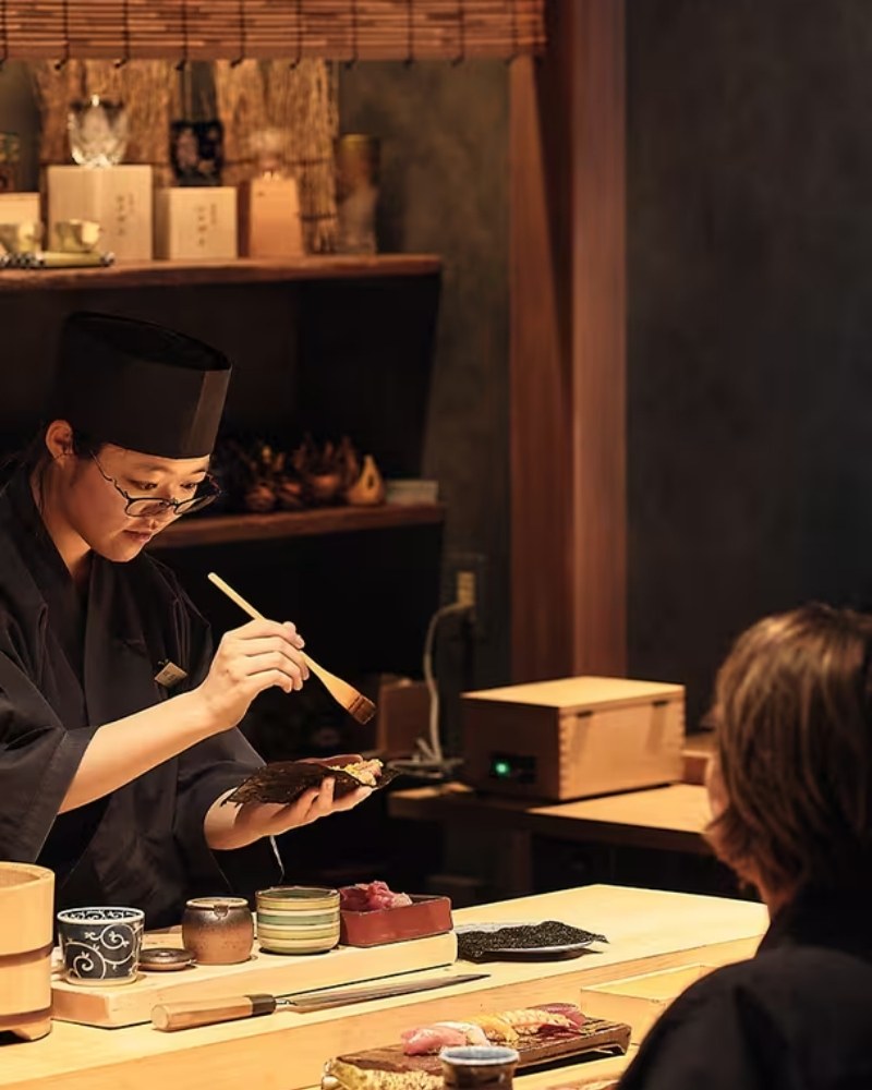 A chef preparing sushi at a counter for a guest