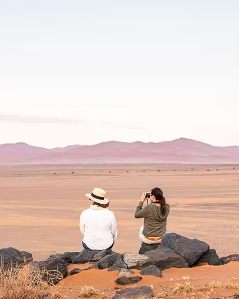 Two travelers sitting on rocks looking across a desert