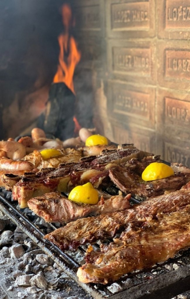 Cuts of beef sizzling on a wood-fired asado grill