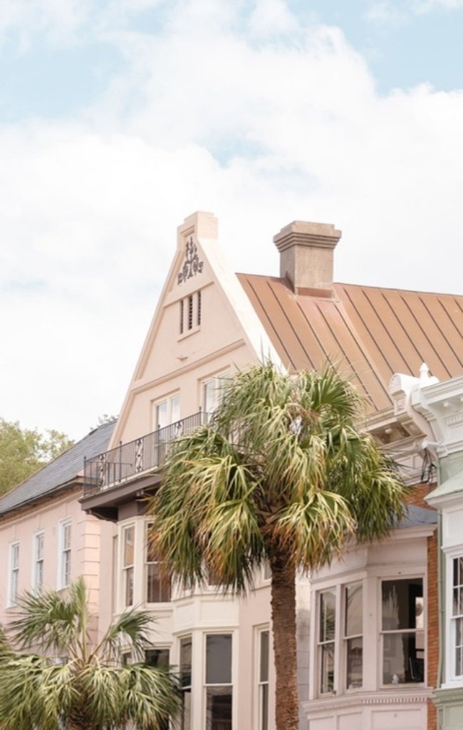 A pastel townhouse with piazzas behind palmetto trees