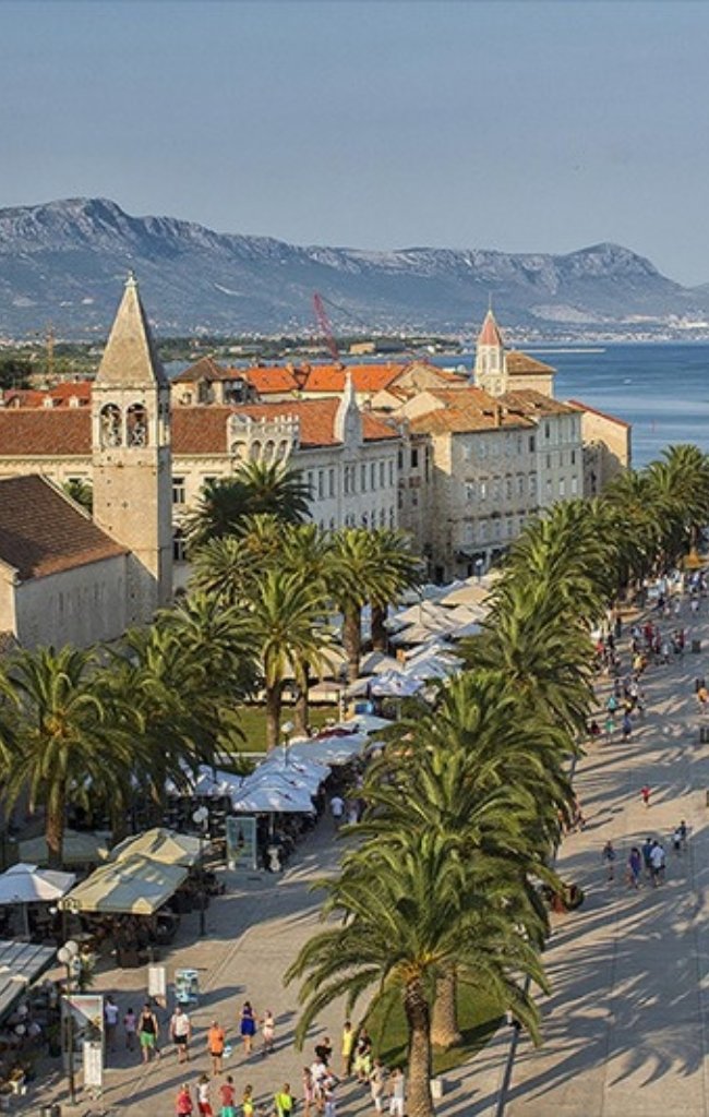 Palm-lined waterfront promenade below the old town of Trogir
