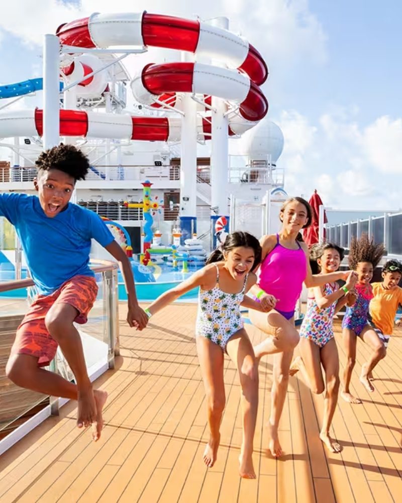 Children running across a pool deck below the waterslides