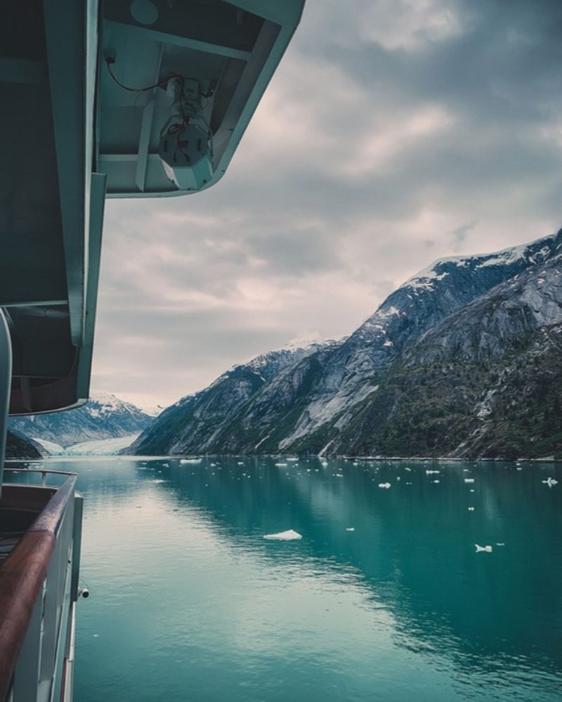 Snowy mountains above a calm Alaska fjord, seen from a ship