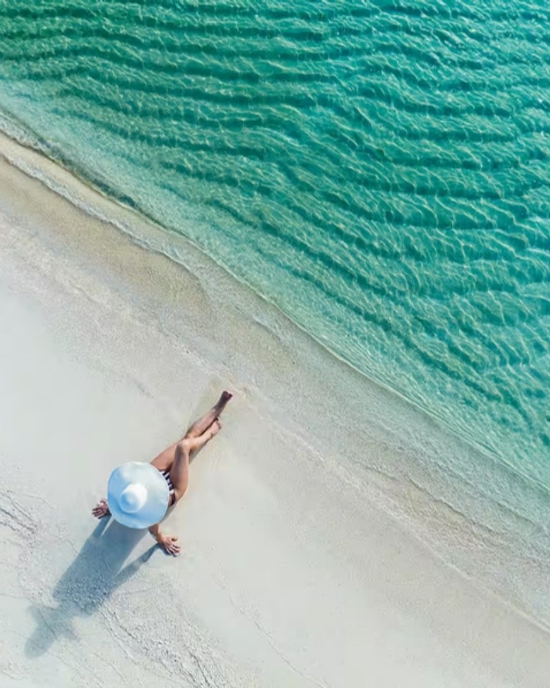 Aerial view of a woman in a sun hat on a white-sand beach