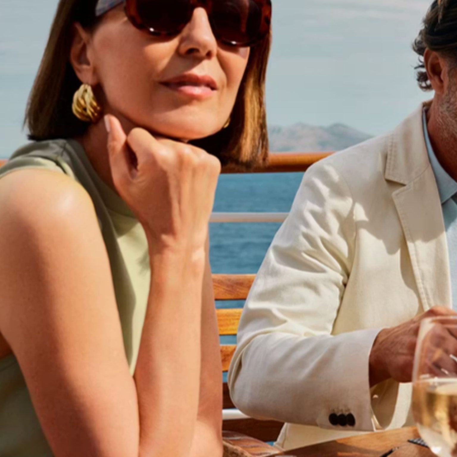 A couple relaxing with glasses of wine on a ship's deck by the sea