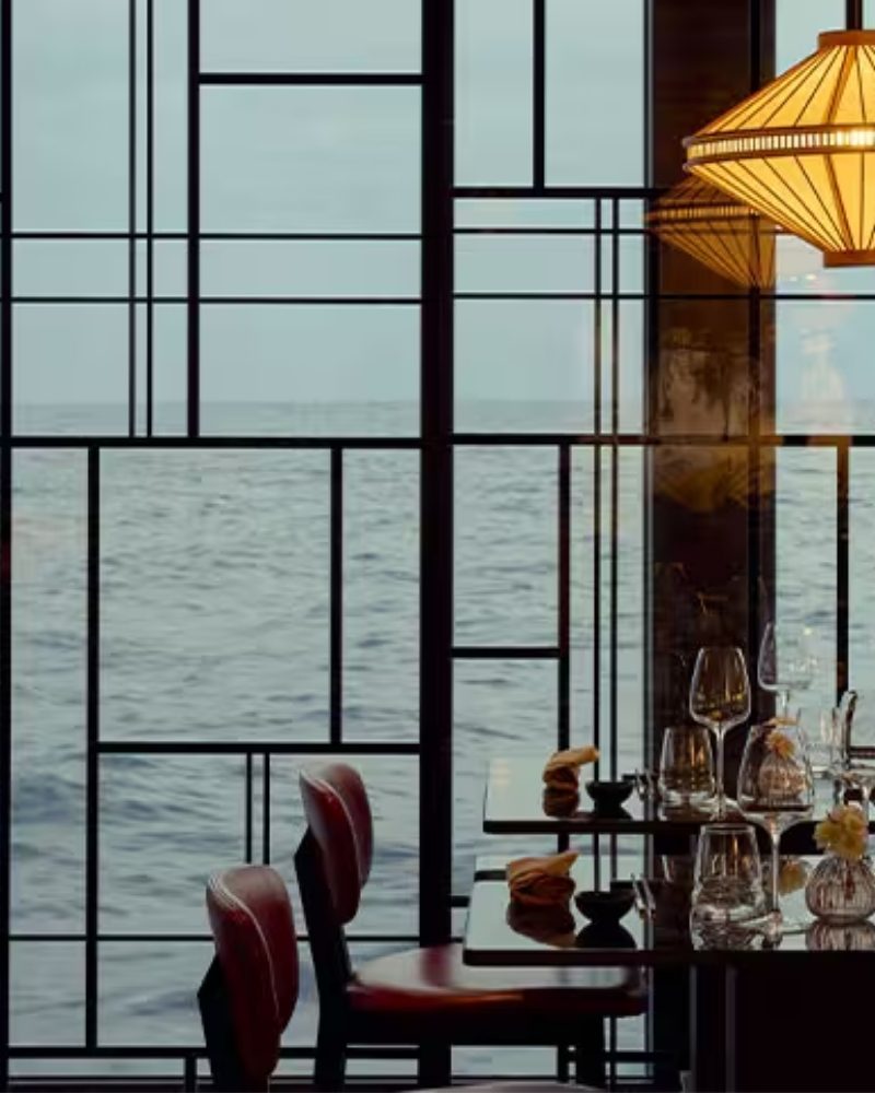 Restaurant tables beside floor-to-ceiling windows overlooking the sea