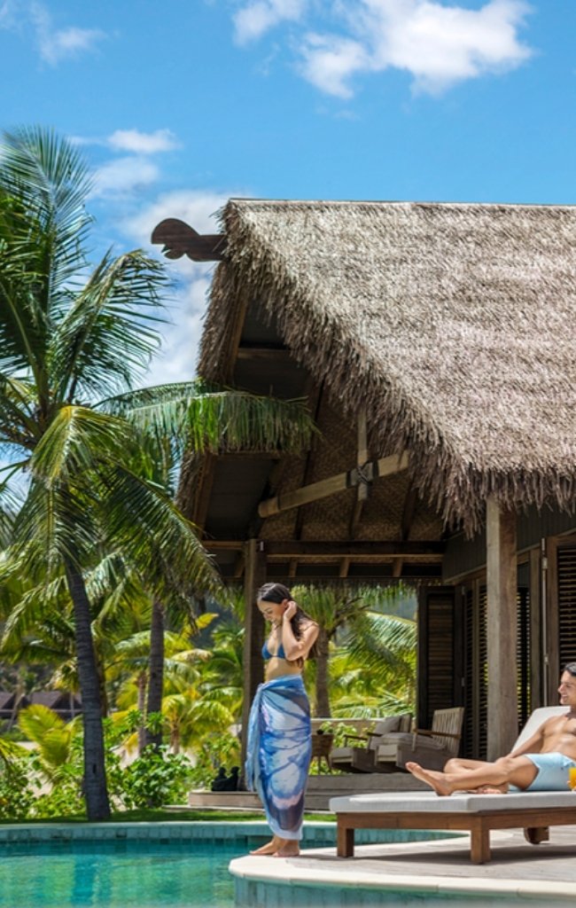 Guests relaxing by a pool beside a thatched villa