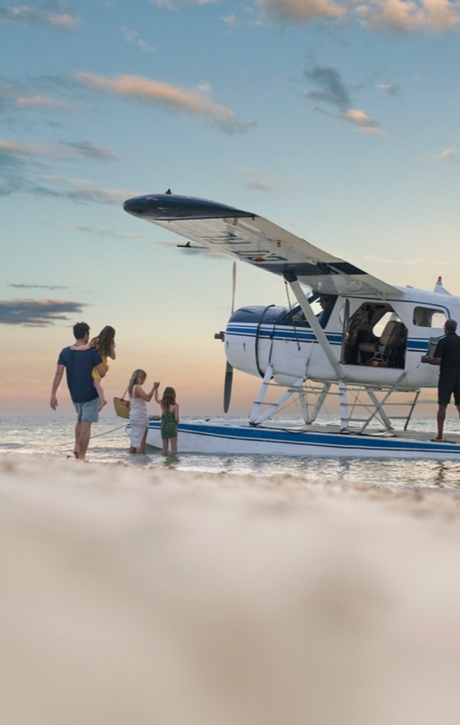 A family walking from a seaplane on a sandbar at sunset
