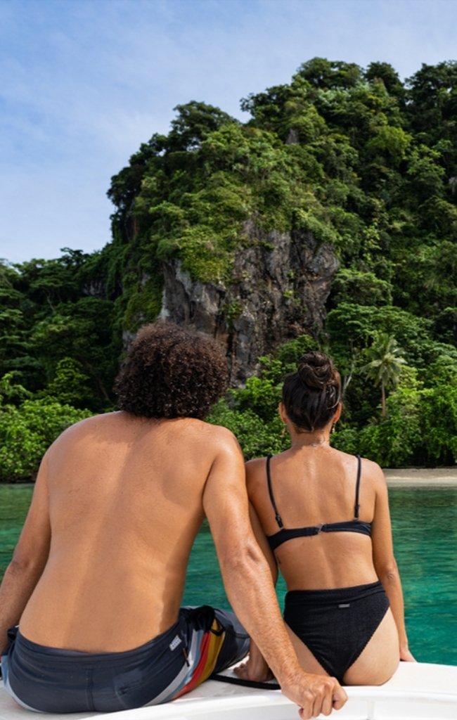 A couple on a boat facing green limestone cliffs and turquoise water