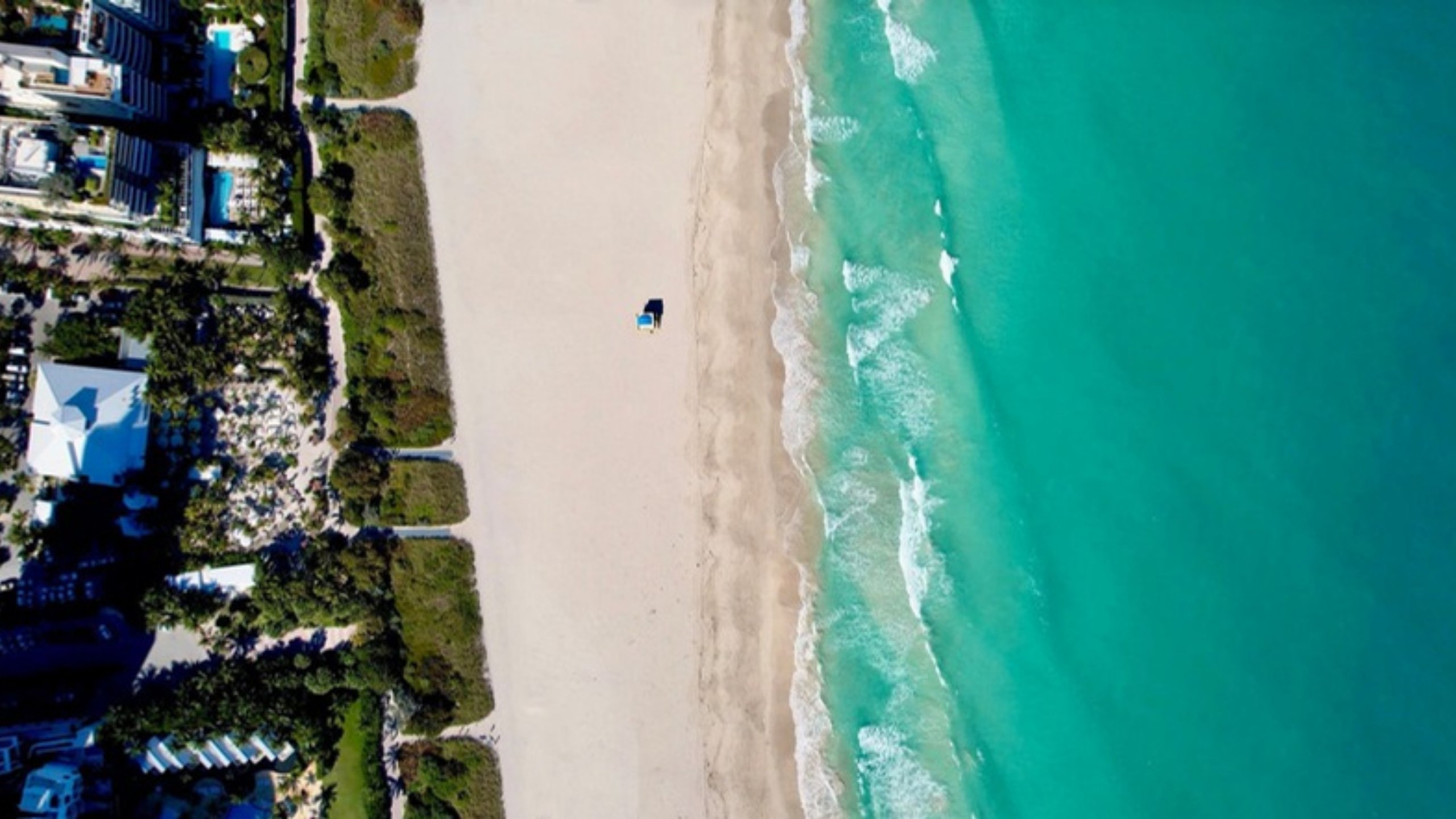 An aerial view of a white sand beach and turquoise water in Miami Beach