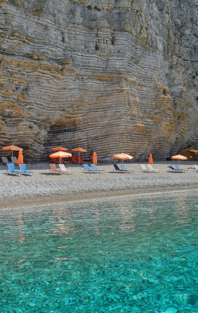 Sun loungers below layered limestone cliffs on a Corfu beach
