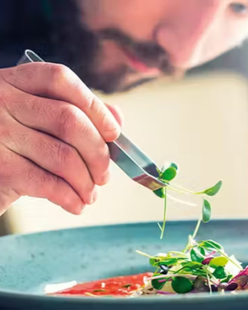 A chef plating a dish with fresh herbs
