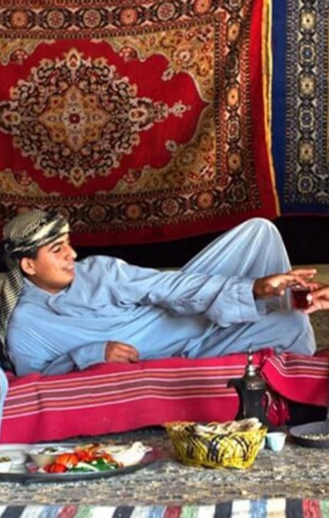Bedouin hosts serving tea to a guest in a carpeted tent
