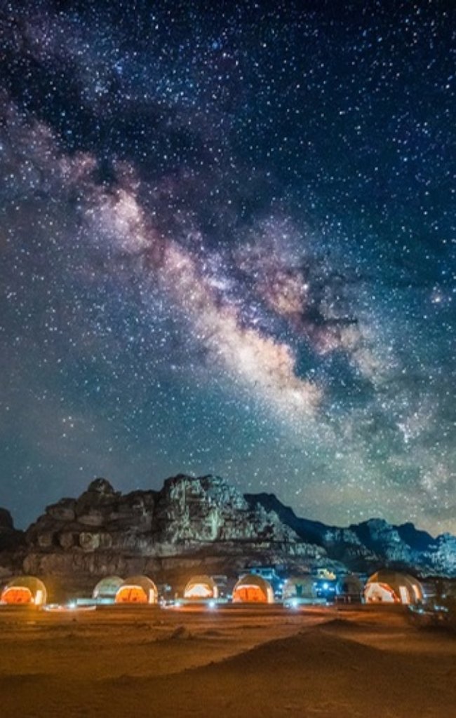 The Milky Way above sandstone cliffs and a desert camp