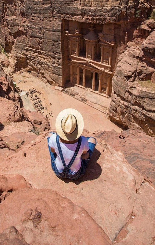A traveler in a sun hat looking down on the Treasury at Petra