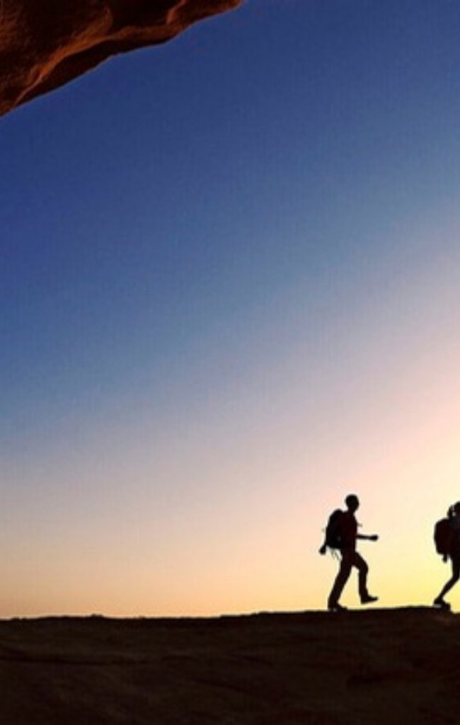 Hikers silhouetted on a sandstone ridge in Wadi Rum at dusk