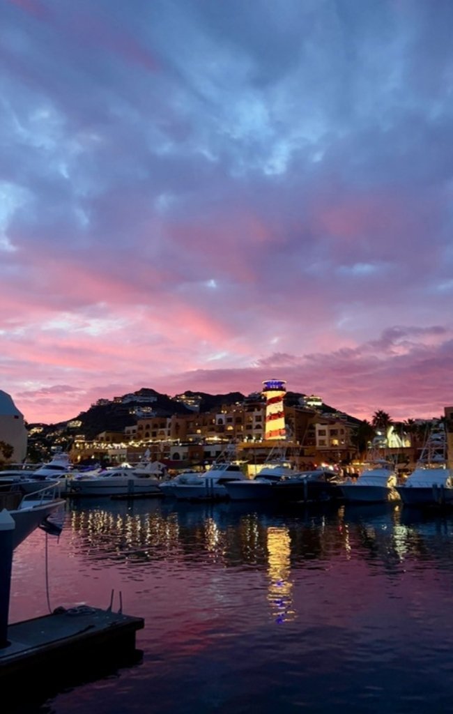 Yachts in the Cabo San Lucas marina under a pink sunset sky