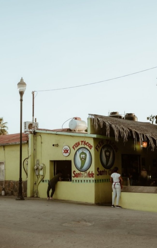 A fish taco stand with a palm-thatch roof on a sunny street
