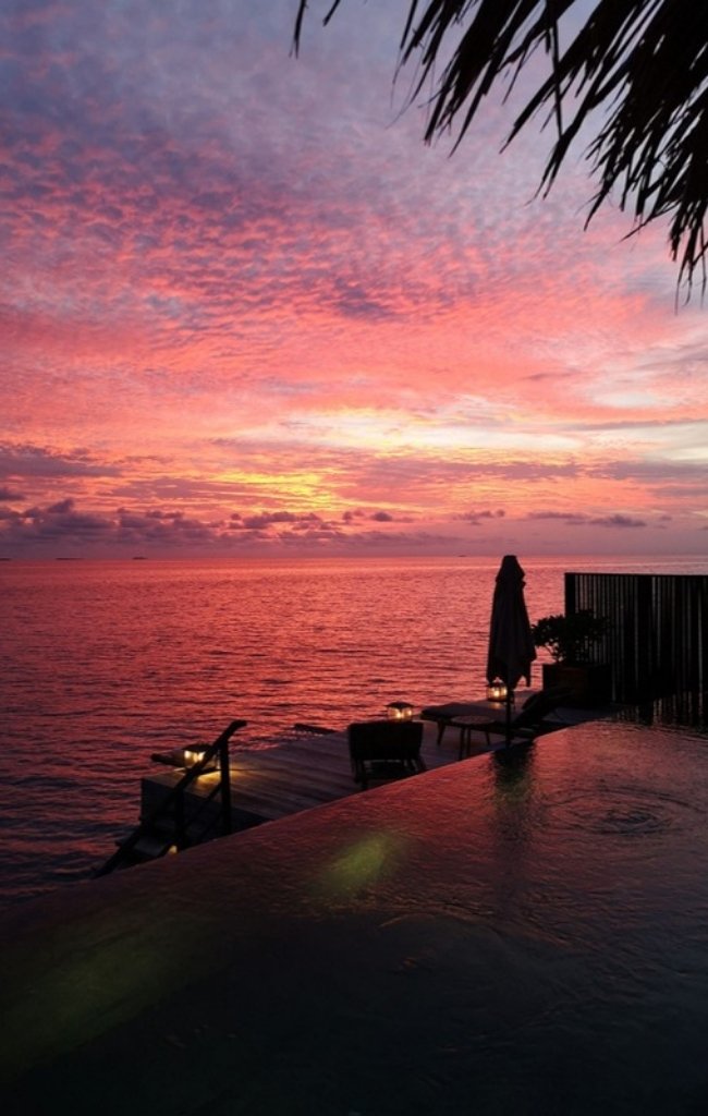 An infinity pool by the sea under a pink sky
