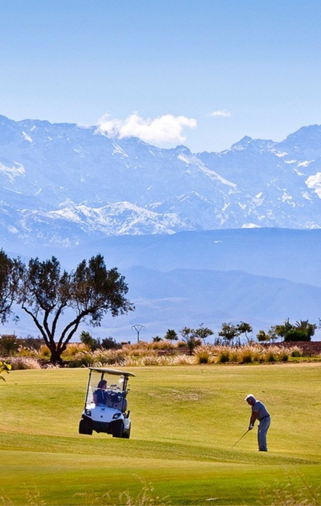 A golfer on a green course with the snowy Atlas Mountains behind