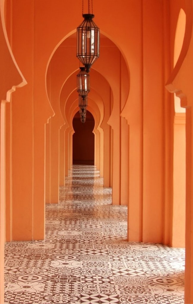 A corridor of terracotta arches and lanterns in a Moroccan palace