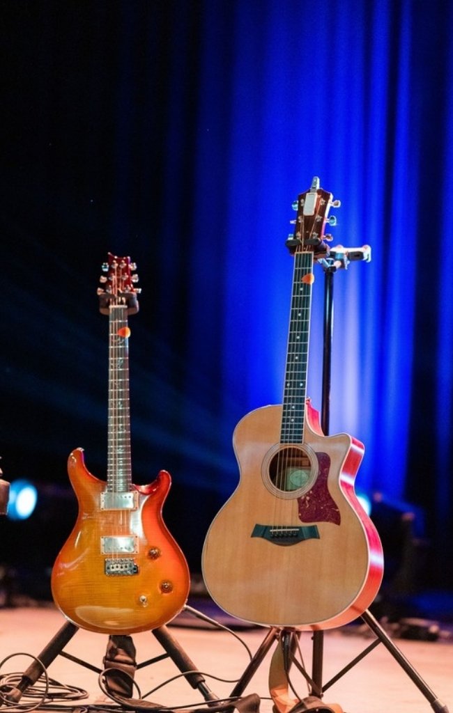 An electric and an acoustic guitar on stands under stage lights