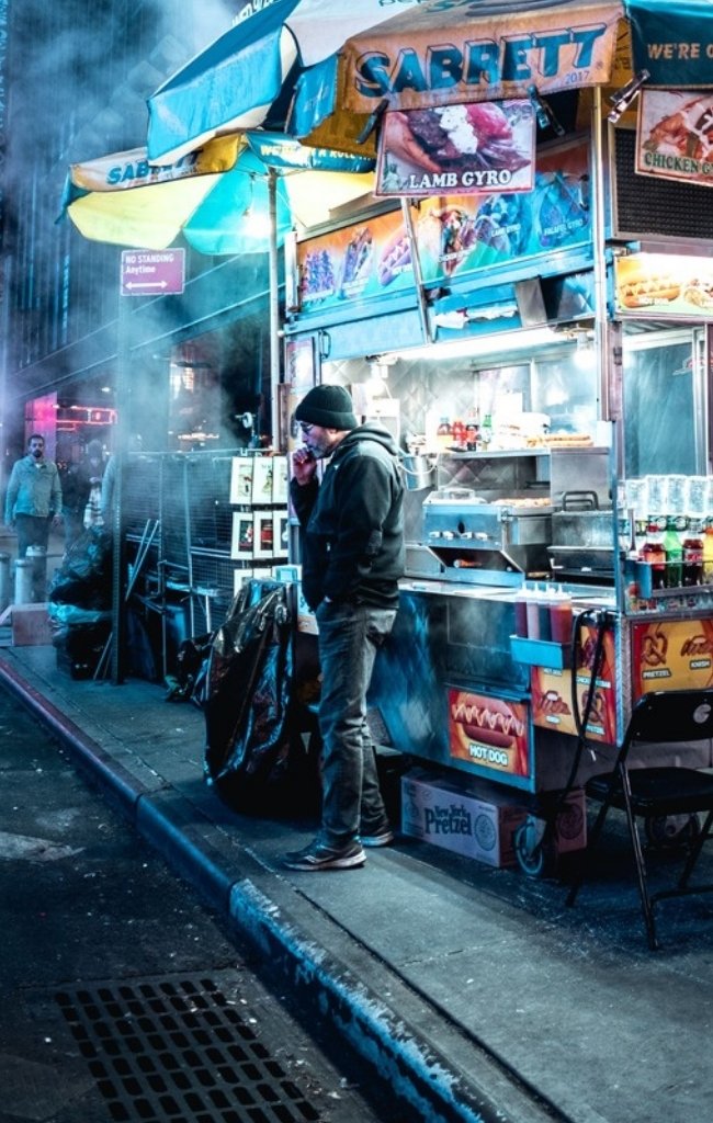 A street food cart glowing on a Manhattan sidewalk at night