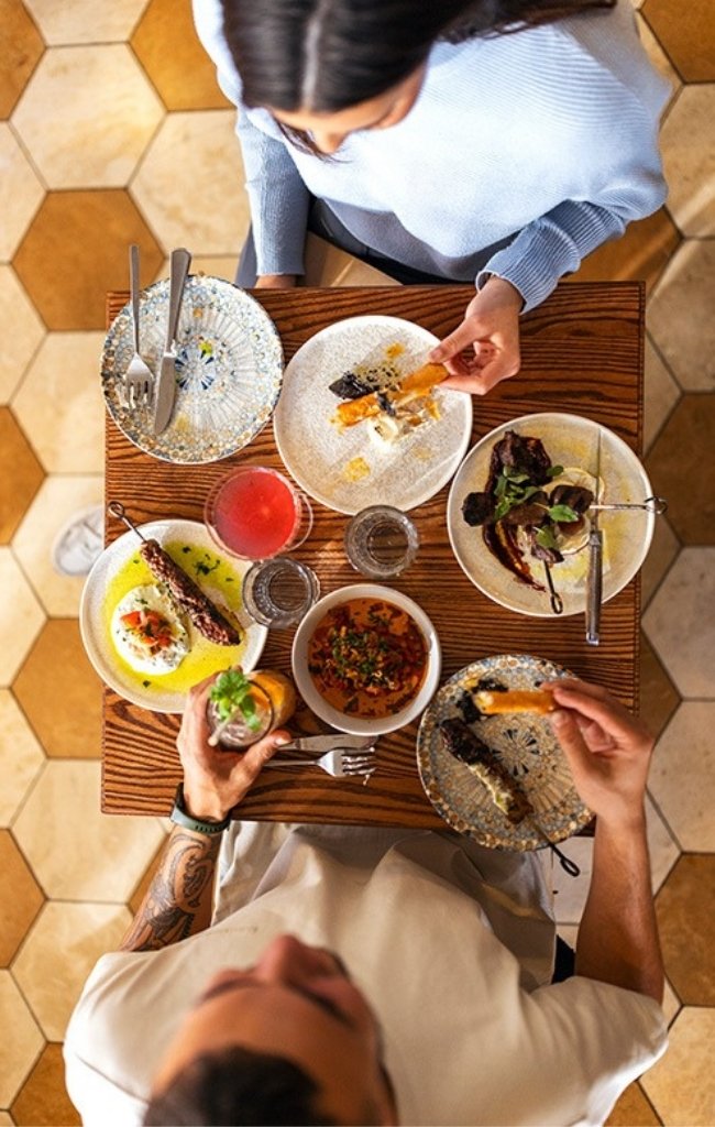 Friends sharing plates of food at a tiled table