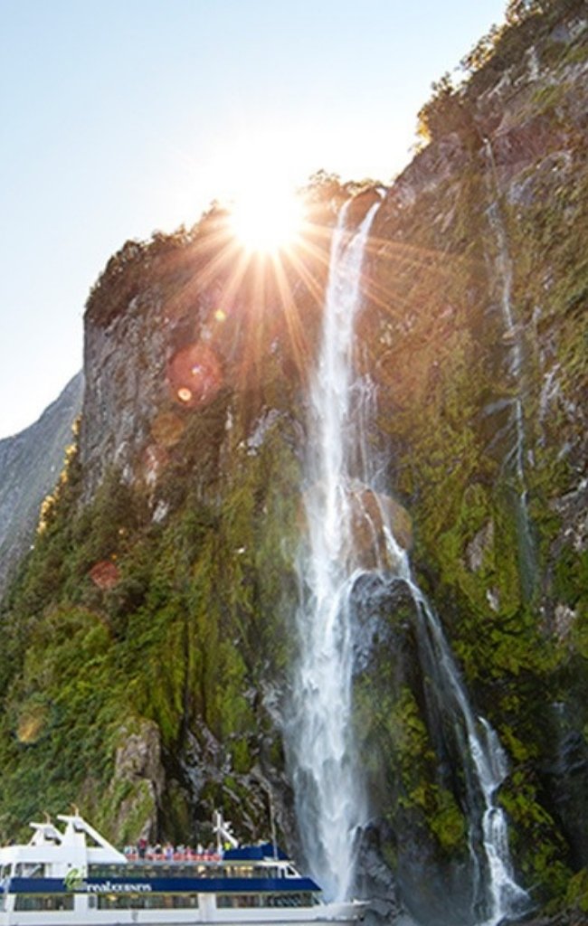 A waterfall pouring down a cliff beside a cruise boat in Fiordland