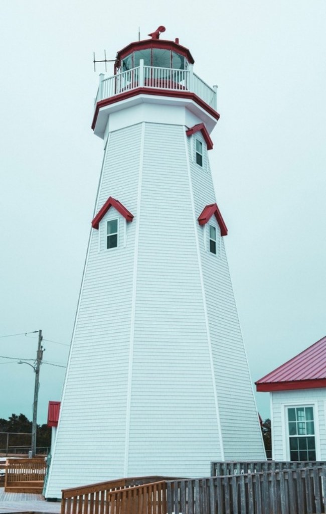A white lighthouse with red trim under a pale blue sky