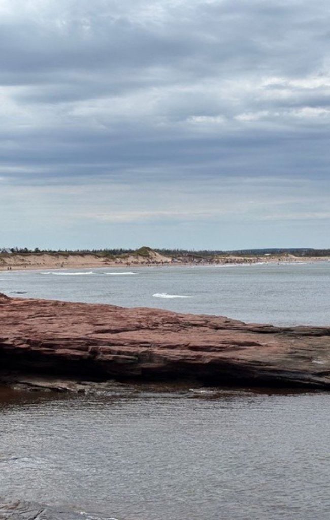 Cavendish Beach with red rocks below a cloudy sky