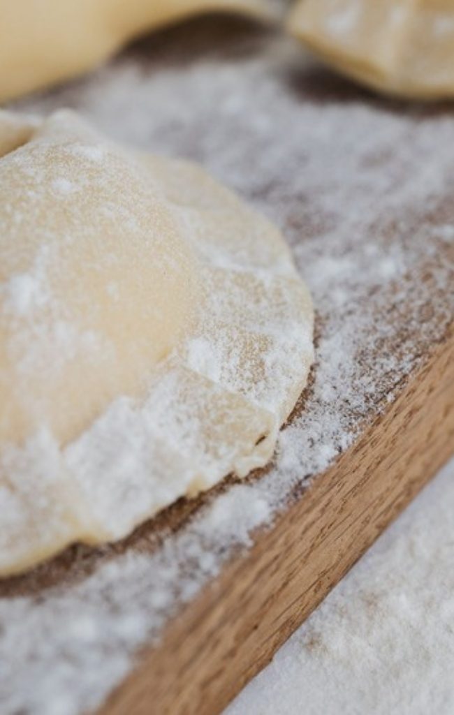 Handmade pierogi dusted with flour on a wooden board