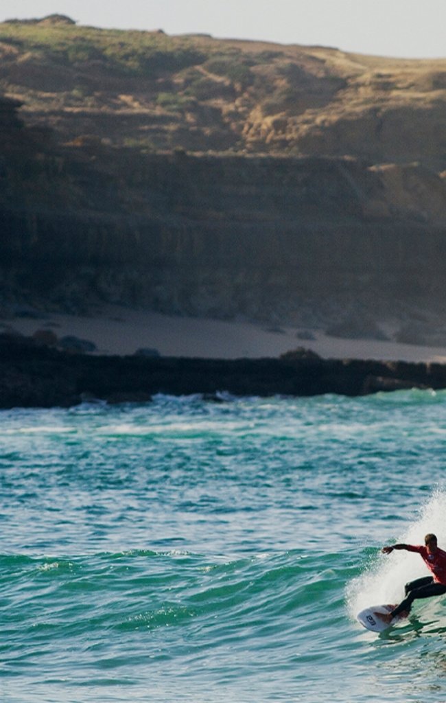 A surfer riding a wave below cliffs on the Portuguese coast