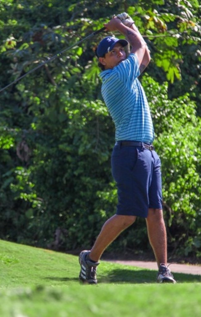 A golfer finishing a swing on a tropical course