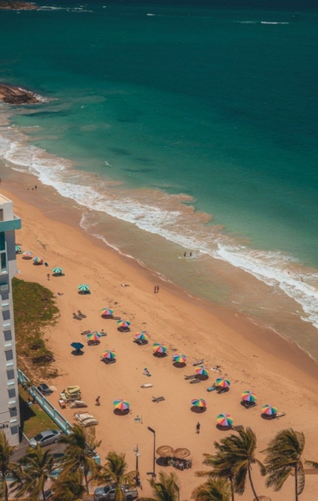 Sun loungers along a golden beach below a high-rise hotel in San Juan