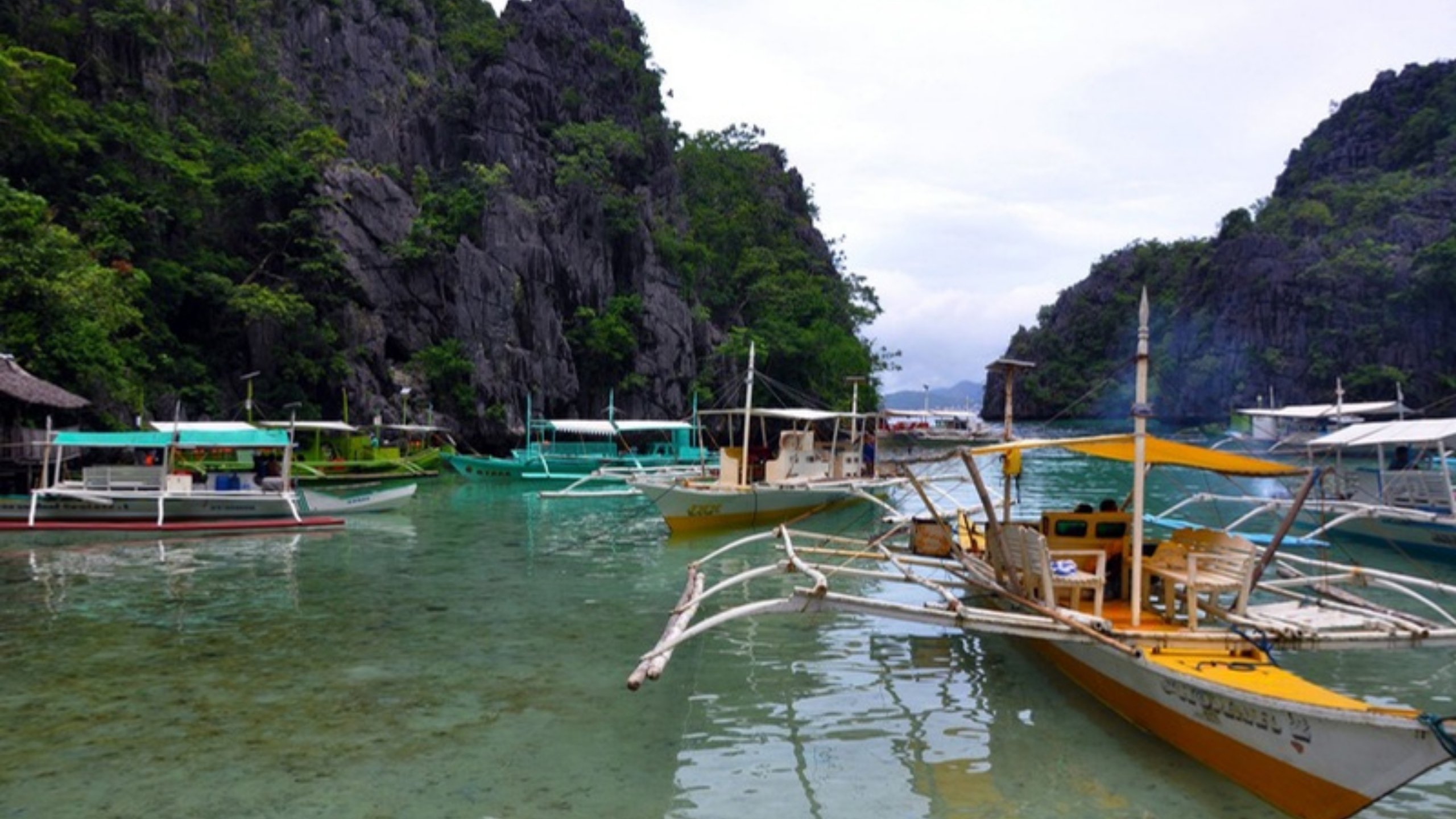 Traditional boats on clear water below green limestone cliffs in El Nido
