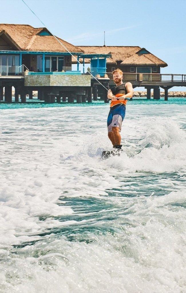 A wakeboarder on turquoise water near overwater villas