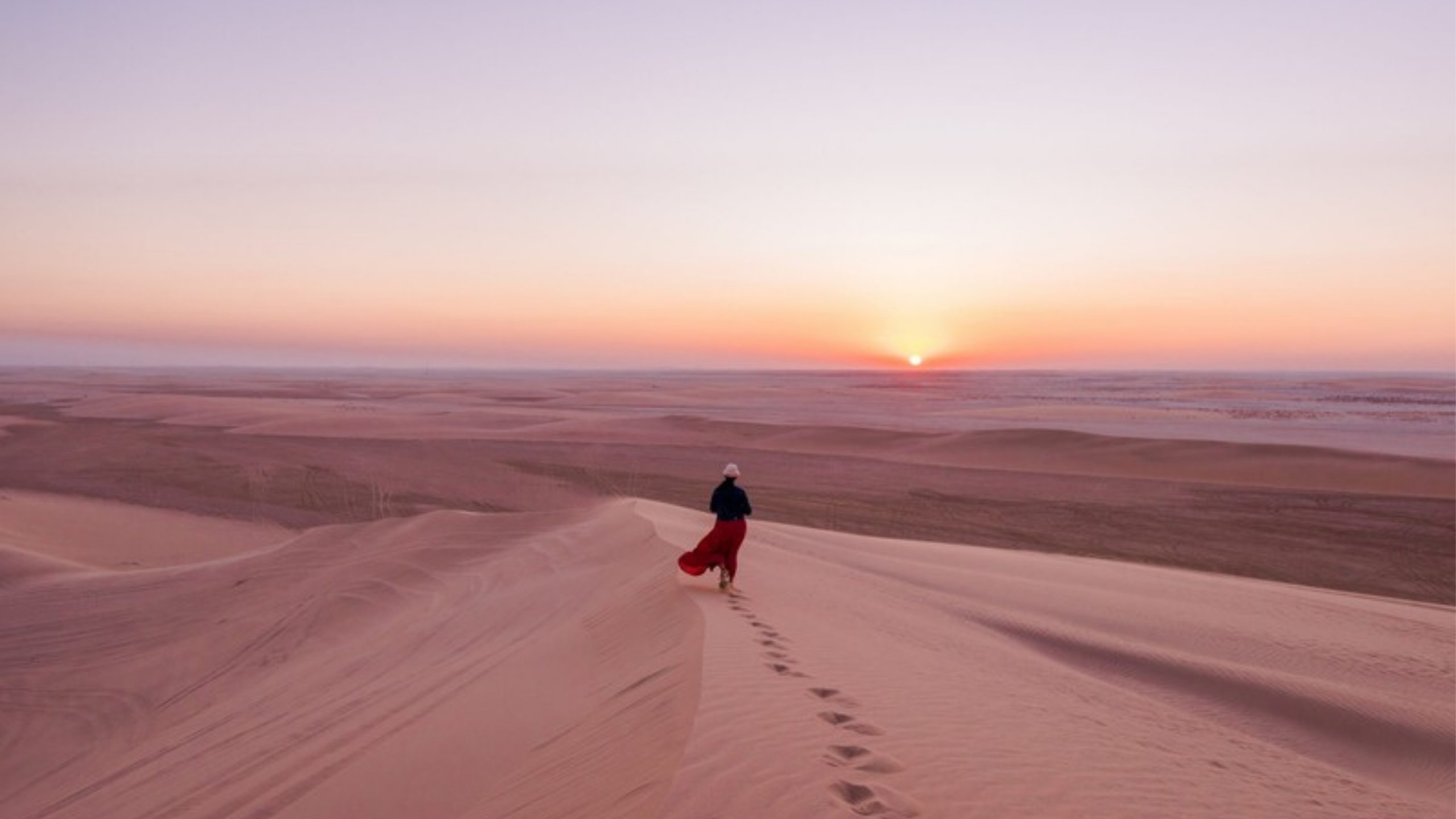 A traveler walking across desert dunes at sunset in Qatar