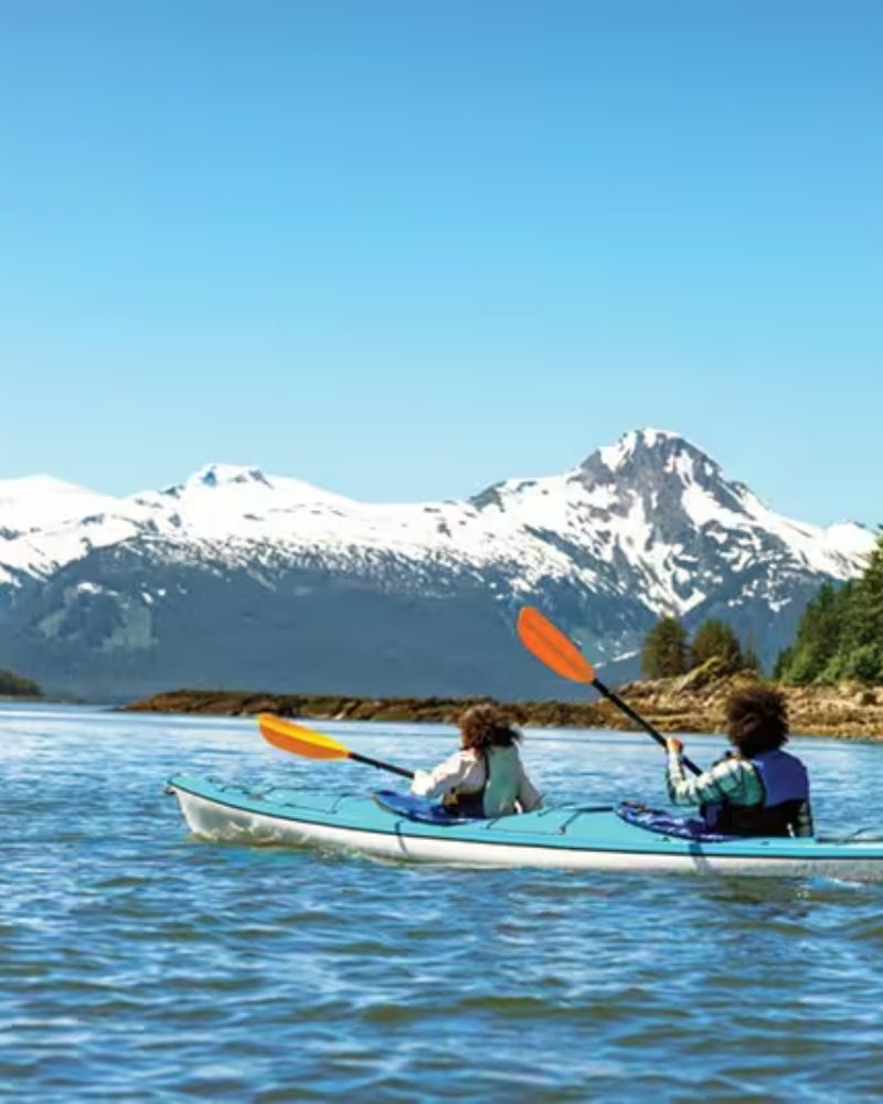 Two people kayaking below snow-capped mountains near Juneau