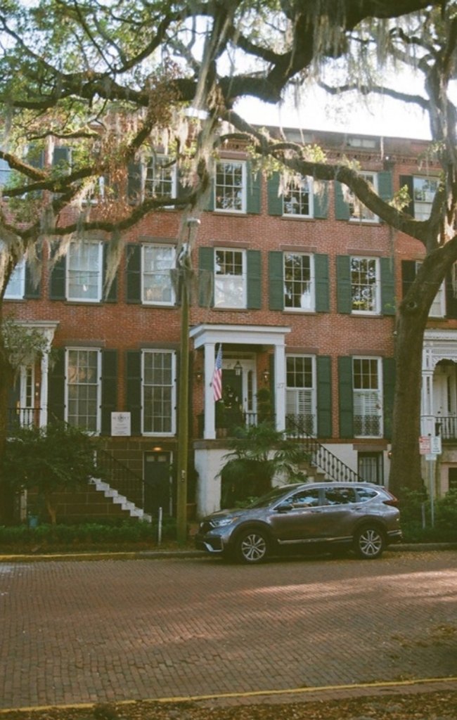 A red-brick Federal-style townhouse behind live oaks