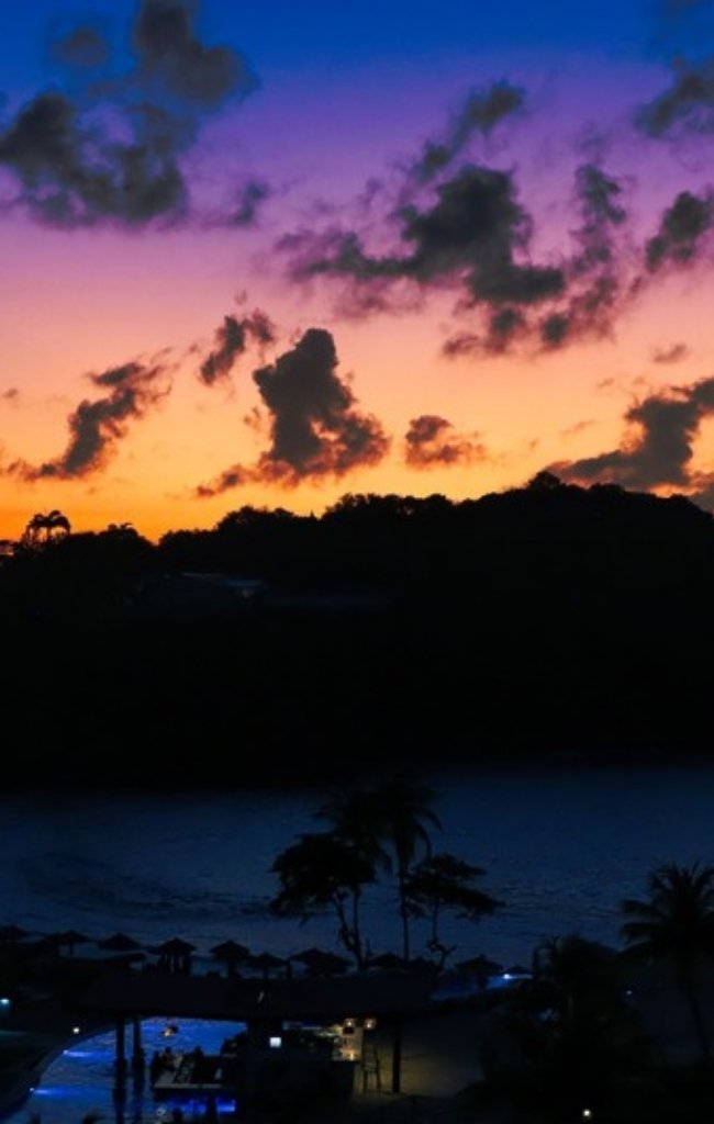 A purple sunset over a resort with palm silhouettes
