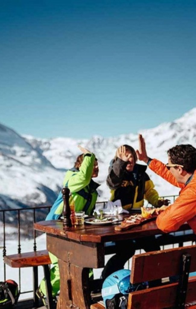 Friends sharing lunch on a sunny mountain terrace above snowy peaks