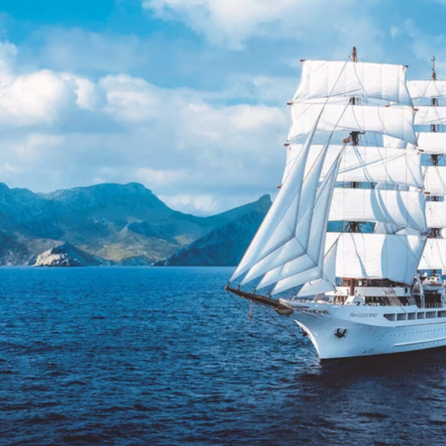 The Sea Cloud Spirit under full sail near a rocky coast