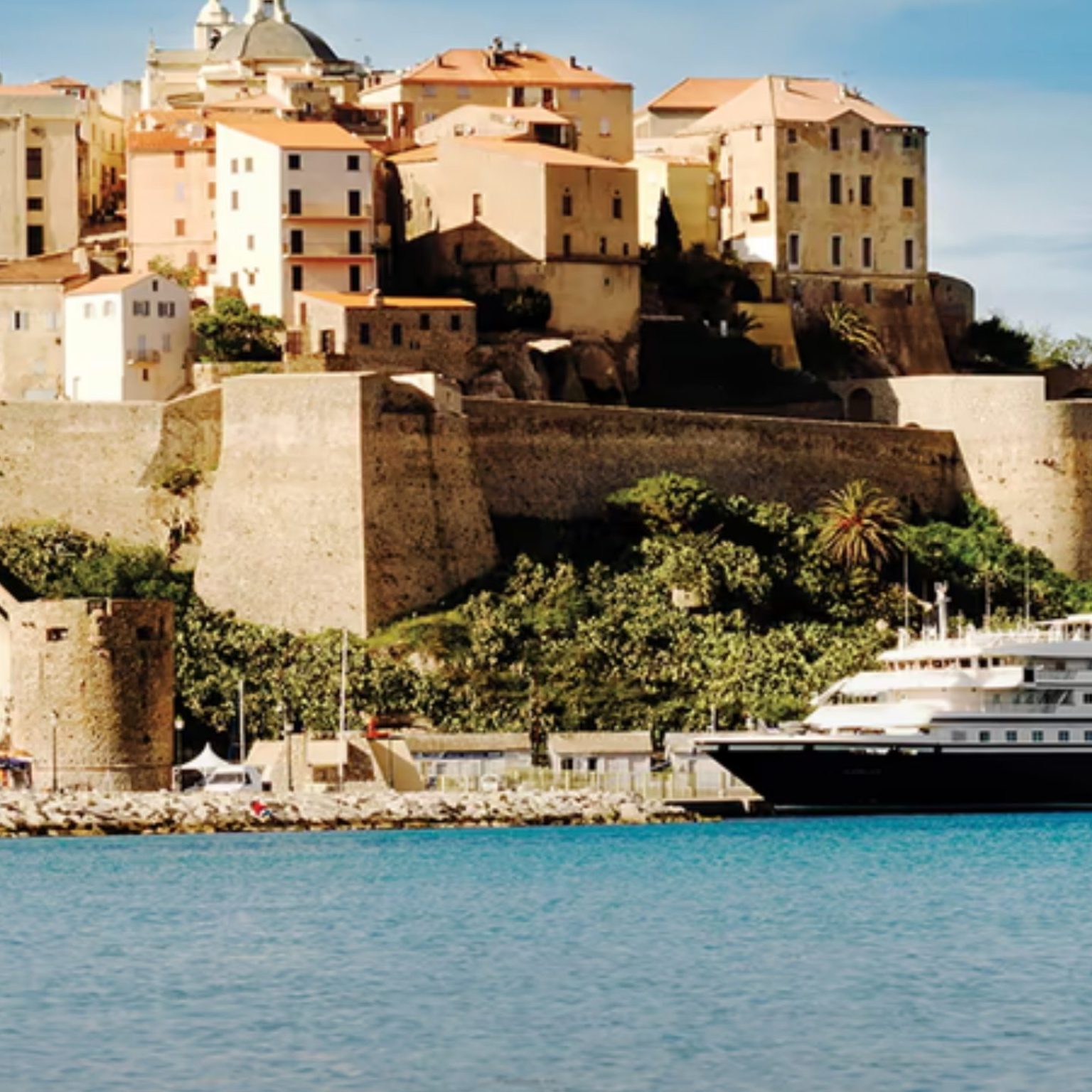 A SeaDream yacht in a Mediterranean harbor below a hilltop citadel